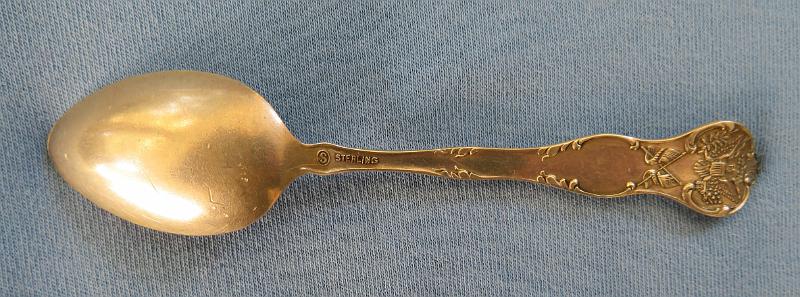 Souvenir Mining Spoon Mizpah Mine Reverse.JPG - SOUVENIR MINING SPOON MIZPAH MINE TONOPAH NV - Sterling silver souvenir demitasse spoon, features handle with miners and marked NEVADA, bowl withdetailed engraving of Mizpah mine scene and marked MIZPAH MINE & MT. BROUGHER at top and TONOPAH across bottom, length 4 1/8 in., marked on reverse Sterling and maker’s mark of S in a circle for Shepard Mfg. Co. MelroseHighlands, MA 1893-1923 (Mt. Brougher is a 6,500 ft. summit just to the west of Tonopah town) [Tonopah is an unincorporated town and the county seat of Nye County, Nevada. It is located approximately midway between Las Vegas and Reno.  One of the richest booms in the west occurred at Tonopah Springs on May 19, 1900. And the name Jim Butler will forever be associated with the name Tonopah and the many stories that surround the discovery. The legendary tale of discovery says that he went looking for a burro that had wandered off during the night and sought shelter near a rock outcropping. When Butler discovered the animal the next morning, he picked up a rock to throw at it in frustration, noticing that the rock was unusually heavy. He had stumbled upon the second-richest silver strike in Nevada history. News of the discovery traveled to the Klondike and soon scores of eager prospectors were searching the area. But it was not until August 27, 1900 that Butler and his wife filed on eight claims near the springs, six of which were some of the biggest producers the state has ever had including the Desert Queen, Burro, Valley View, Silver Top, Buckboard, and Mizpah, the largest silver producer in the district. Because the Butler claims were known far and wide, the town was often referred to as Butler. By the summer of 1901, the mines around the town produced nearly $750,000 worth of gold and silver. Now it was time for a post office and one opened on April 10, 1901 named Butler.  By 1902 Jim Butler had sold his claims, which were all consolidated and gave birth to a new company, the Tonopah Mining Company. It was incorporated in Delaware, with stock listed on both the Philadelphia and San Francisco exchanges. The company, with J.H. Whiteman as president, controlled 160 acres of mineral-bearing ground around the Tonopah district. The company also had holdings in the Tonopah-Goldfield Railroad and controlled mining companies in Colorado, Canada, California and Nicaragua. The mine workings at Tonopah consisted of three deep shafts with more than 46 miles of lateral workings. The deepest of the three shafts was 1,500 ft. The ore mined at the site was treated in a 100-stamp mill. Also in 1902 the Tonopah-Belmont Mining Company was formed and was based in New Jersey with C.A. Heller as president. The company’s property, 11 claims covering more than 160 acres, was on the east side of the property owned by the Tonopah Mining Company. There were two deep vertical shafts, 1,200 and 1,700 ft, with workings covering almost 39 miles.  Butler now had a population of 650 and was increasing every day. It also had six saloons, restaurants, assay offices, lodging houses, and a number of doctors and lawyers. It was not until March 3, 1905 that its name was changed to Tonopah. By 1907, Tonopah had become a full-fledged city with modern hotels, electric and water companies, five banks, schools, and hundreds of other buildings. Tonopah’s mines continued to produce extremely well until the Depression brought a slowdown. From 1900 to 1921, they produced ore worth almost $121 million. Tonopah’s biggest year was 1913 when its mines yielded almost $10 million worth of gold, silver, copper, and lead. By the time World War II started, only four major mining companies were operating in Tonopah. At the end of the war even the companies that had been there at the beginning were gone. In 1968, Howard Hughes and his Summa Corporation bought 100 claims in Tonopah, including the Mizpah, Silver Top, and Desert Queen mines. Hopes for a mining revival soon faded after disappointing core samples were taken. A few of the old mines were re-timbered but never reopened. The value of the Tonopah district’s total production is just over $150 million.  Today tourism plays a large part in the local economy.]